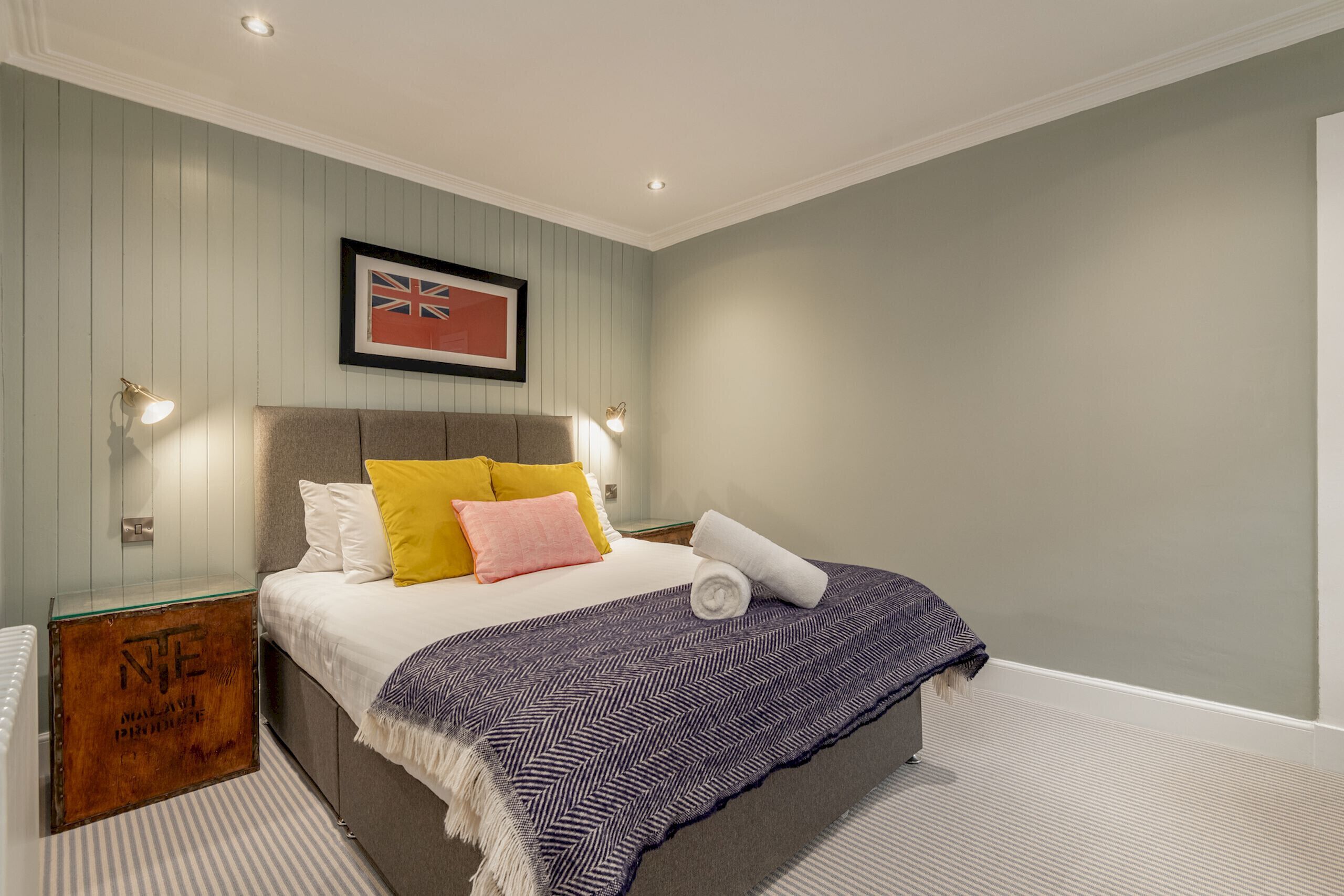 Een keurig opgemaakt slaapkamer met een bed, kussens, een deken, een lijst met een vlag en een klein houten doosje.