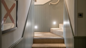 Un escalier recouvert d’une moquette à motifs tissés, un tableau encadré avec un « X » rouge, et une main courante.