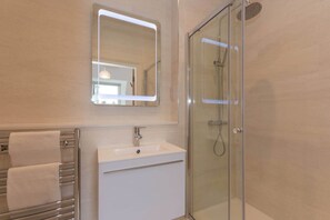 A modern bathroom with a glass-enclosed shower, a white sink, and a mirror with a lighted frame.