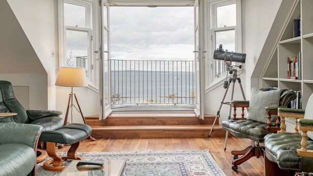 A room with a balcony, leather furniture, a telescope, and a bookshelf. - Gillespie Apartments | Spectacular Penthouse (St Andrews)