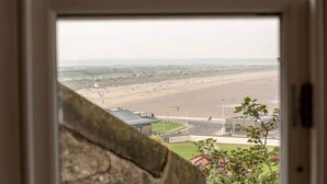 A view through a window of a beach with a road and buildings in the foreground. - Gillespie Apartments | Spectacular Penthouse (St Andrews)