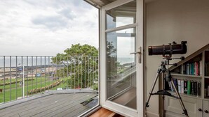 A balcony with a telescope, a view of the sea, and a bookshelf with books. - Gillespie Apartments | Spectacular Penthouse (St Andrews)