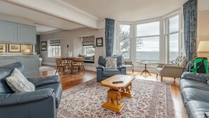 A spacious living room with a large window, a dining area, and a kitchen. - Gillespie Apartments | Golfer's Dream (St Andrews)