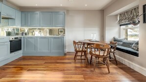 A modern kitchen with light blue cabinets, a wooden dining table, and chairs. - Gillespie Apartments | Golfer's Dream (St Andrews)