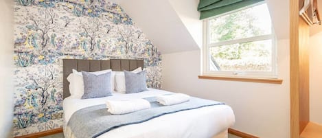 A bedroom with a large bed, a headboard, a window with curtains, and a wall with a floral wallpaper.