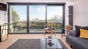 Un salon moderne doté d’une grande porte-fenêtre coulissante donnant sur un balcon, d’un canapé, d’un fauteuil, d’une petite table et d’une plante en pot.