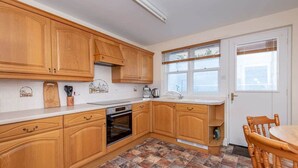 Een keuken met houten kastjes, een betegelde vloer en een raam met zonwering.