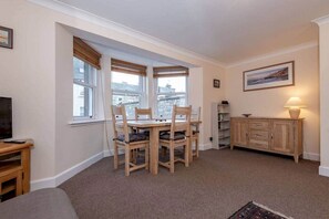 A cozy living room with a wooden dining table and chairs, a television, and a bookshelf.