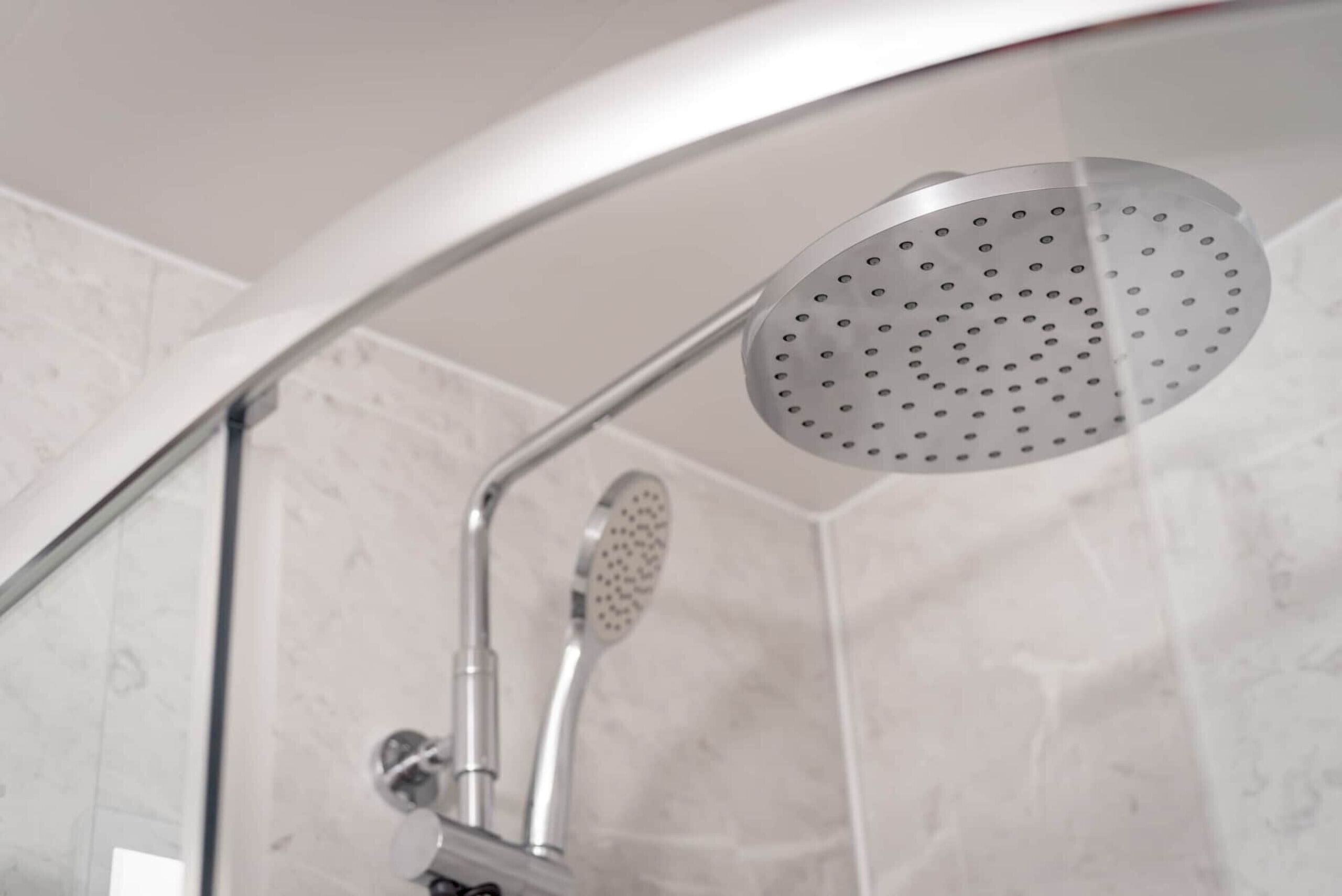 Eine Dusche mit einer gebogenen Glasduschwand und einer Handbrause.