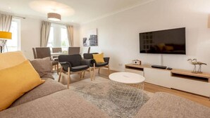 A modern living room with a sofa, chairs, a coffee table, a TV, and a dining area. - Abbey Villa (No 5) (St Andrews)