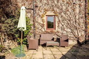 A patio with wicker furniture, a table, and an umbrella. - Old Mill Cottage (Dunino)
