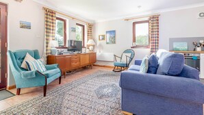 A living room with a sofa, armchairs, a television, and a dining area with a table and chairs. - Old Mill Cottage (Dunino)