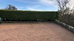 A gravel-covered outdoor area with a stone wall and a neatly trimmed hedge. - Old Mill Cottage (Dunino)