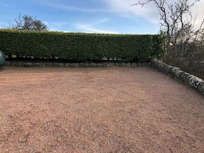 A gravel-covered outdoor area with a stone wall and a neatly trimmed hedge. - Old Mill Cottage (Dunino)