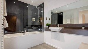 Et moderne badeværelse med et glasbad, et hvidt badekar og et stort spejl.