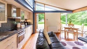 Une cuisine moderne dotée d’un four et d’une cuisinière encastrés, un coin repas avec une table et des chaises en bois, et une grande fenêtre offrant une vue sur la verdure.