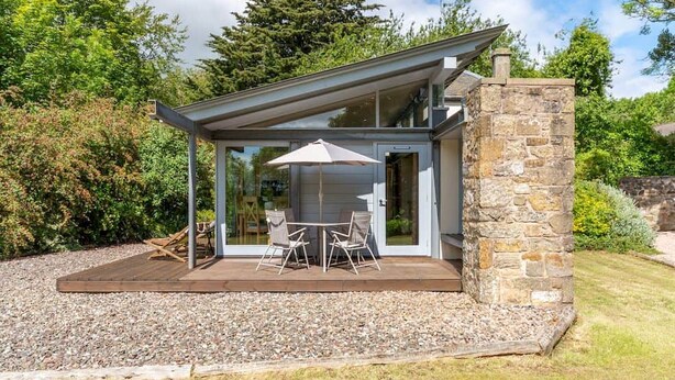Une maison moderne dotée d’un patio, d’un espace salon extérieur et d’un mur en pierre.