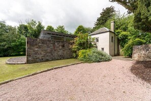 A stone wall, a gravel driveway, and a building with a chimney.
