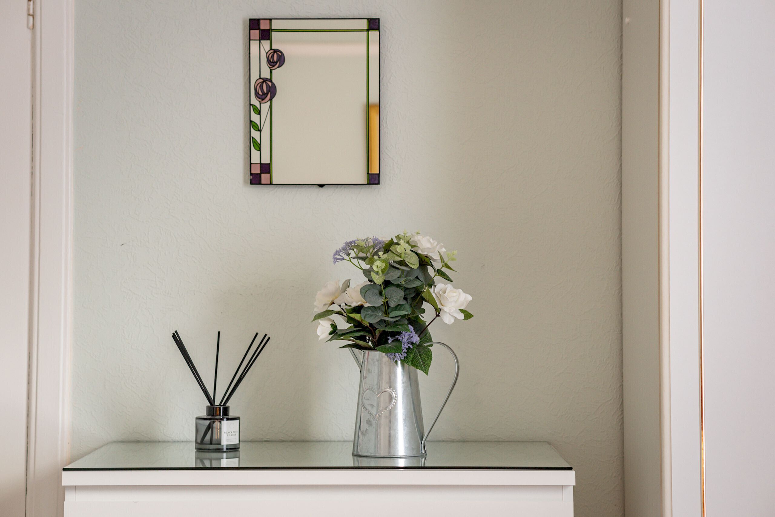 A small table with a clear glass vase containing white flowers and a metal candle holder.
