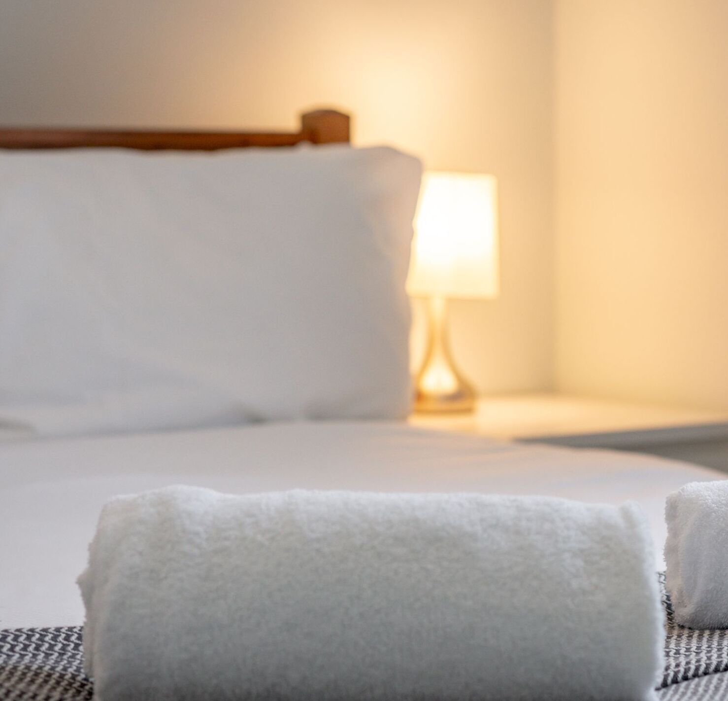A bed with white linens, a wooden headboard, and a bedside lamp.
