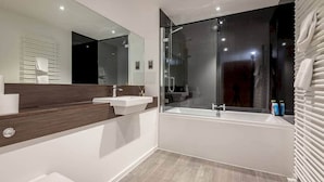 Une salle de bain moderne avec un grand miroir, deux lavabos, une baignoire et une douche à l’italienne.