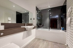 A modern bathroom with a large mirror, two sinks, a bathtub, and a glass-enclosed shower.