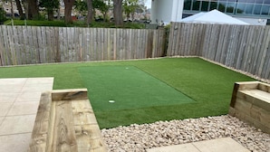 Un jardin avec une pelouse artificielle, une terrasse en bois et un chemin en pierre.