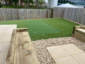 A backyard with artificial grass, a wooden deck, and a stone pathway. - Square Green | Garden Apartment With Putting Gree (St Andrews)