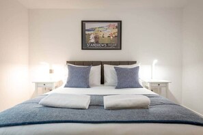 A hotel room with a bed, two bedside tables, and a framed picture on the wall.