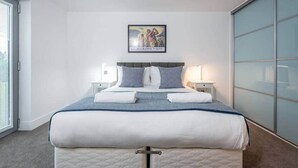 Une chambre moderne avec un grand lit, deux tables de chevet, un tableau encadré au mur et une porte-fenêtre coulissante.