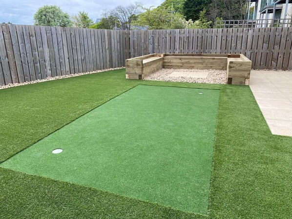 A backyard with artificial green turf, a wooden play structure, and a wooden fence.