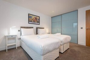 A hotel room with two beds, a large sliding glass door, a framed picture on the wall, and a small bedside table with a lamp. - Square Green | Garden Apartment With Putting Gree (St Andrews)