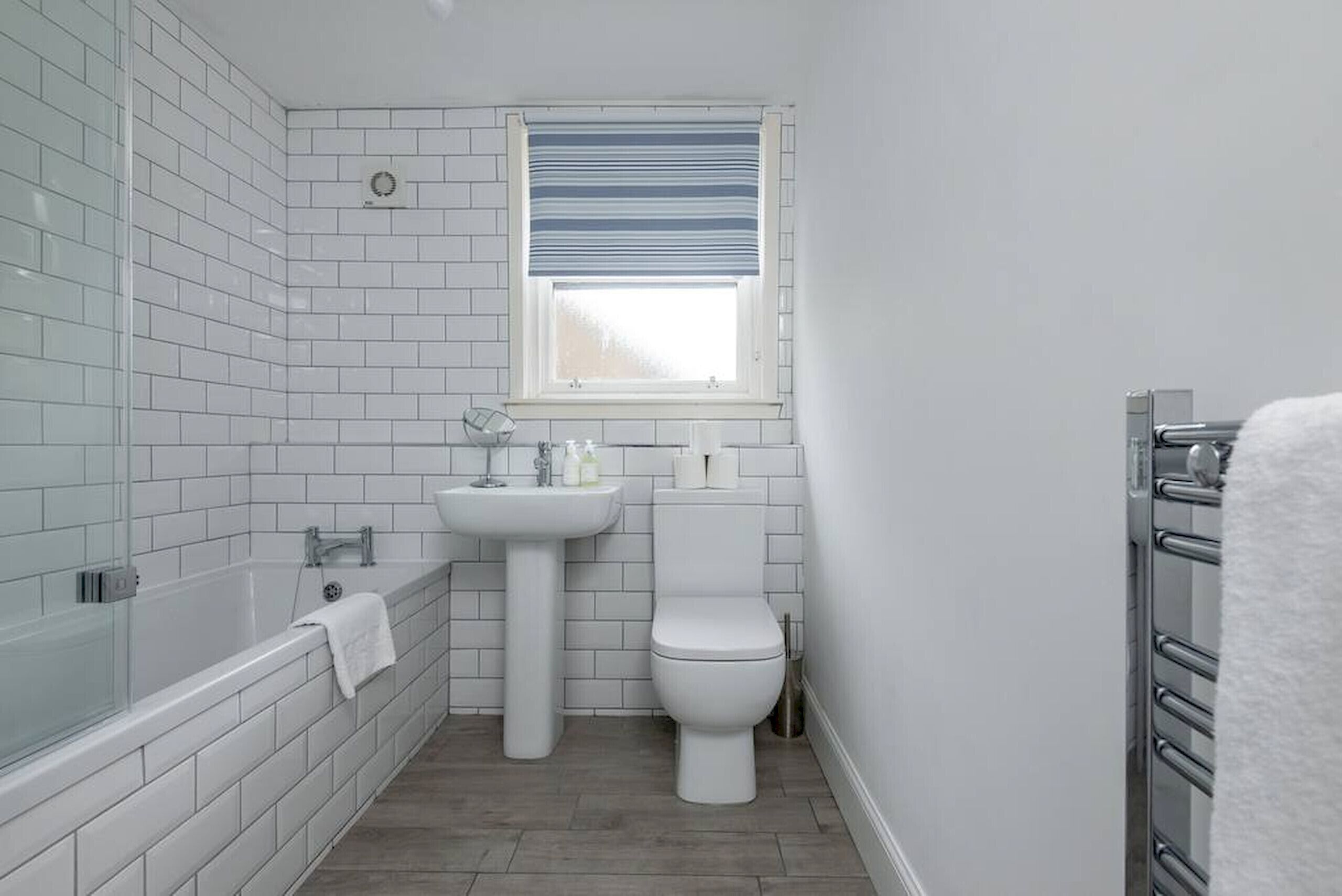 Een badkamer met witte betegelde wanden, een badkuip, een wastafel en een toilet.