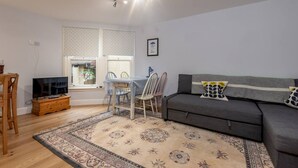 A living room with a sofa, a TV on a wooden stand, a dining table with chairs, and a patterned rug.