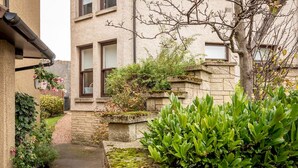 A narrow pathway leading to a building with stone steps and a small garden area with various plants and flowers.