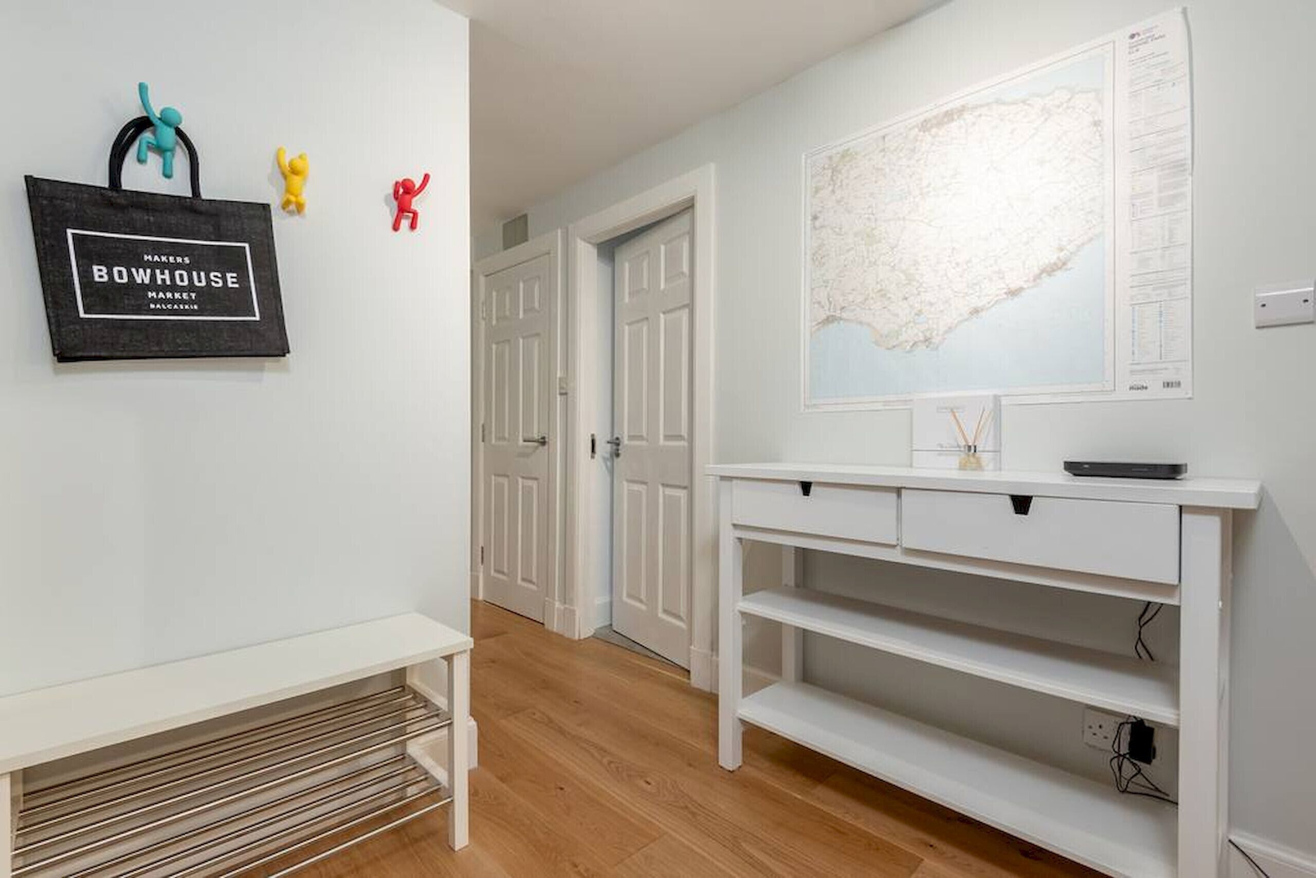 Un couloir avec une console blanche, un panneau encadré et une carte accrochée au mur.