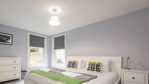 A bedroom with a bed, two nightstands, a dresser, and a window with blinds.