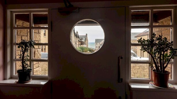 A room with a round window, two potted plants, and a view of buildings outside.