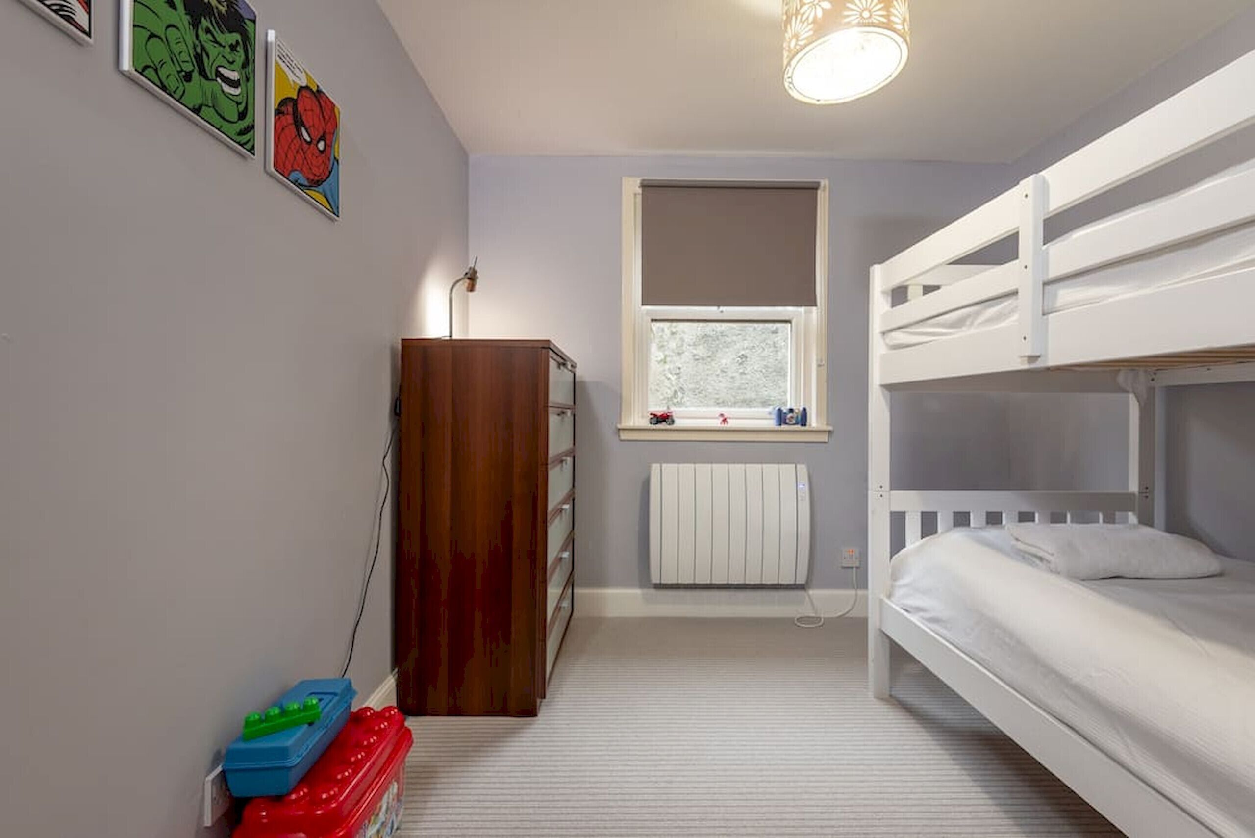 A child's bedroom with bunk beds, a radiator, a window, and a wooden wardrobe.