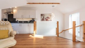 Une cuisine moderne avec des meubles blancs, un plafond en bois et un coin repas comprenant un canapé et un tableau.
