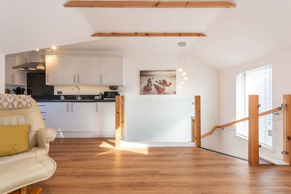 A modern kitchen with white cabinets, a wooden ceiling, and a dining area with a sofa and a painting.