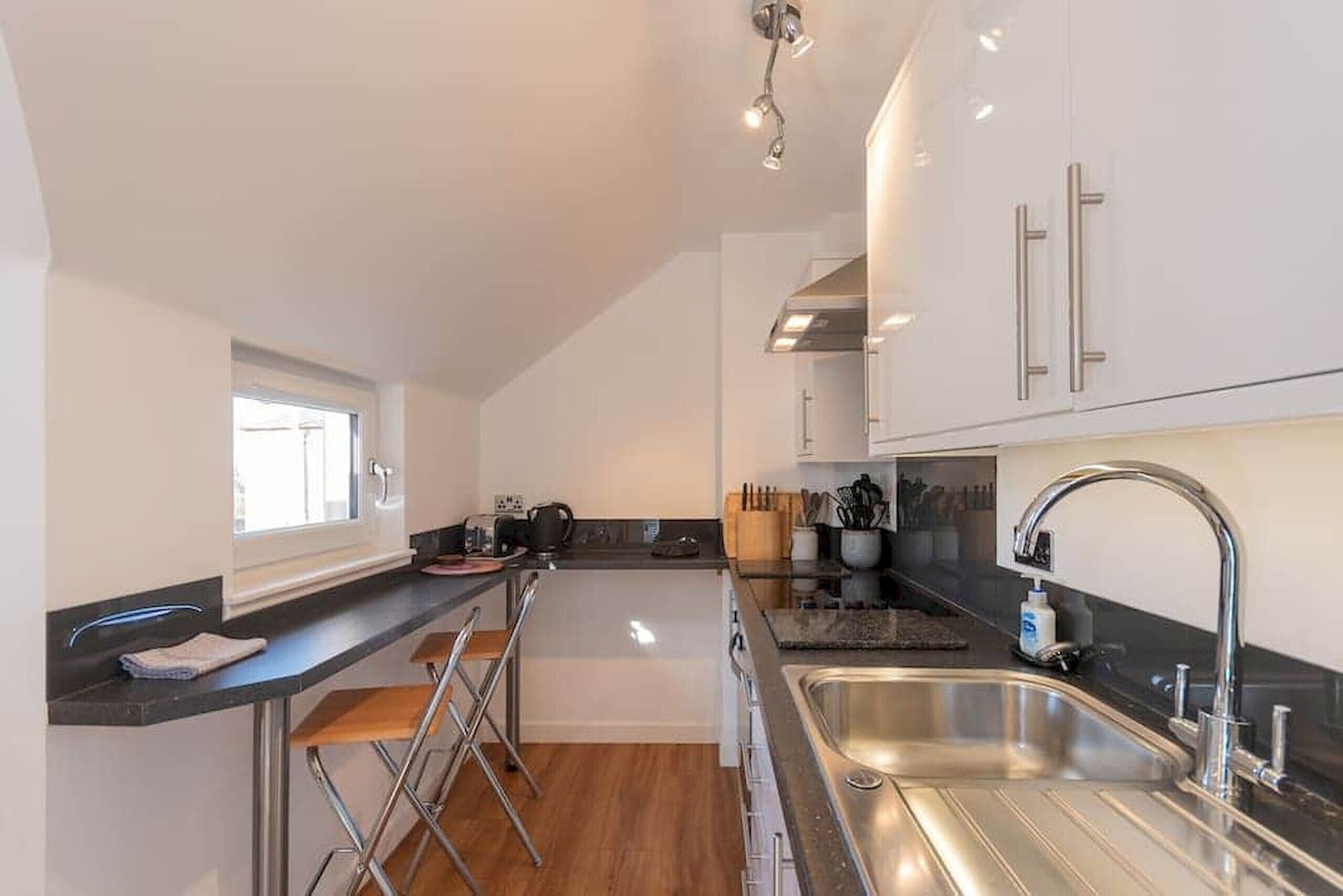 A compact kitchen with a sink, bar stools, and a window.