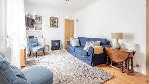 Un salón con un sofá azul, una mesa de centro de madera, un sillón azul, un radiador blanco y una estantería.