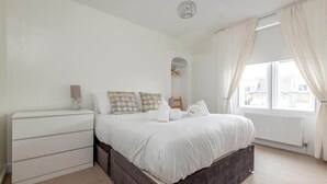 Un dormitorio con cama, cómoda, vestidor y ventana con cortinas.