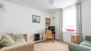 Una sala de estar con sofá, una silla, una mesita, televisor, mueble y ventana con cortinas.