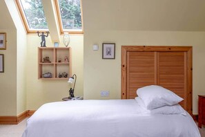 A bedroom with a bed, a skylight, a wooden wardrobe, and a shelf with decorative items. - Muir Park Cottage (Grange)