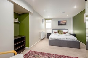 Une chambre à coucher avec un lit, un radiateur, une fenêtre, une étagère et une chaise.