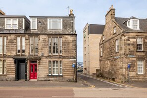 A historic stone building with a red door, a visible sign for 'Plum Links', and a clear blue sky.