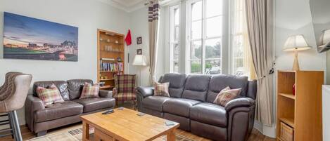 A living room with two leather sofas, a wooden coffee table, a bookshelf, and a painting on the wall.