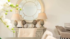A room with a round mirror, two lamps, decorative vases, and a chair. - Village Green | Kingsbarns (Kingsbarns)